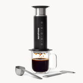 AeroPress Steel coffee maker with a glass mug of coffee on a white background #color_black