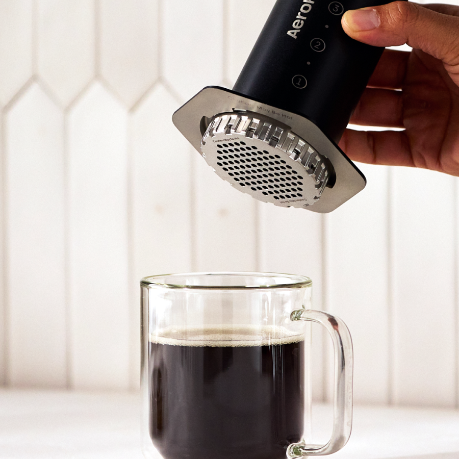 Hand holding a black AEROPRESS device over a glass of coffee. #color_black
