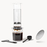 AeroPress coffee maker with a clear container, plunger, and filter on a white background