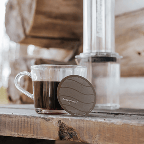 Clear glass mug with coffee and Aeropress filter on a wooden surface