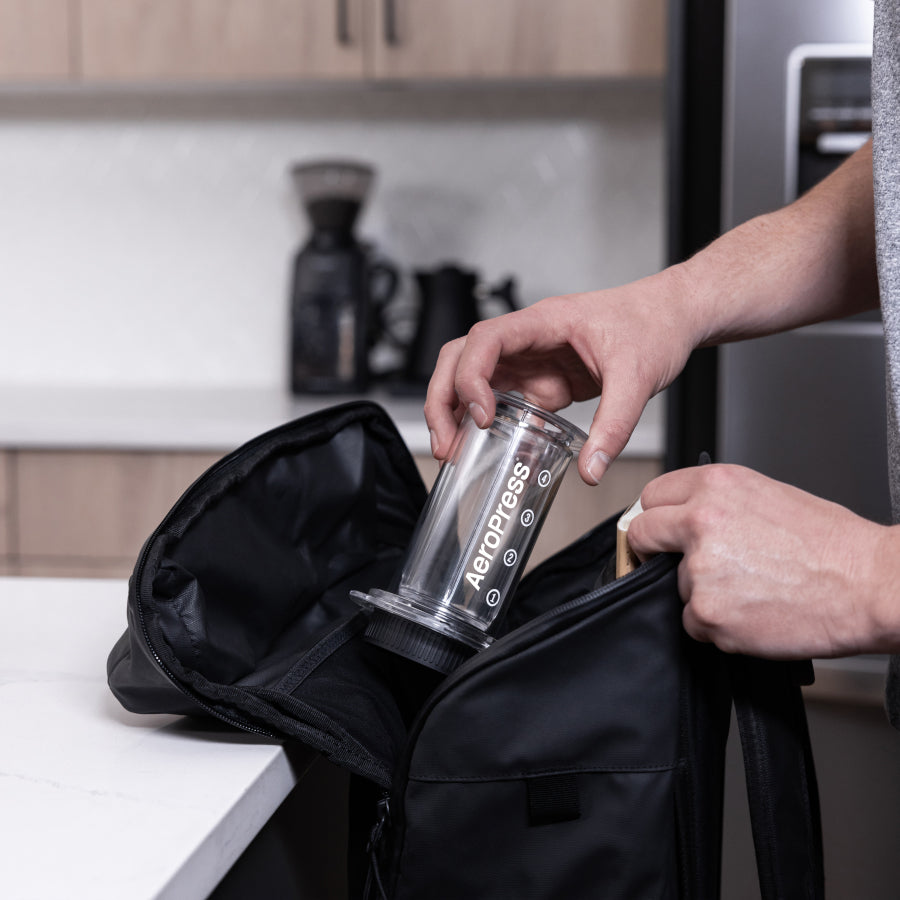 AeroPress Coffee Maker - Clear being placed into backpack #color_clear