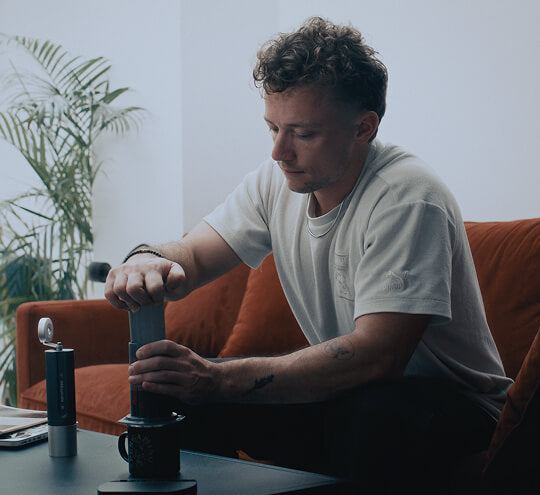 Man using an AeroPress coffee maker in a cozy living room setting.