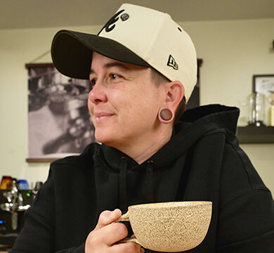 Person wearing a cap and holding a textured mug in a casual setting