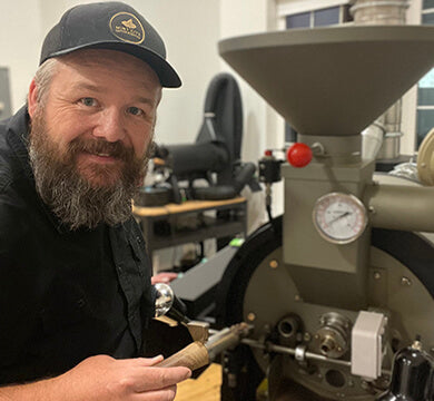 Man with a beard and cap working on a coffee roaster machine.