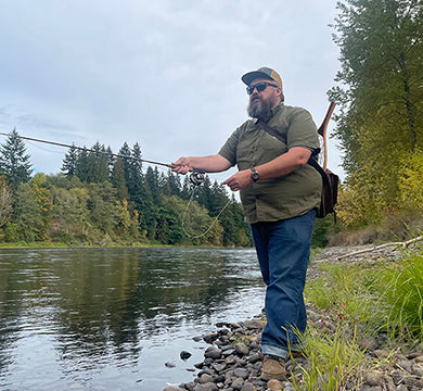 Man fishing by a river with trees in the background