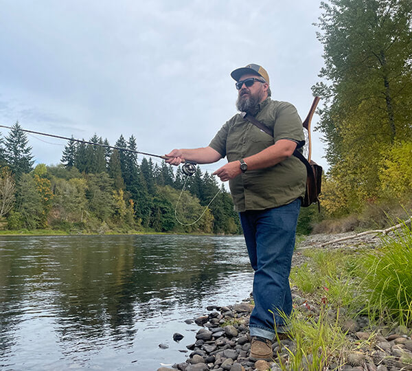 Man fishing by a river with trees in the background