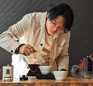 Person preparing coffee using an AeroPress coffee maker in a cozy setting.