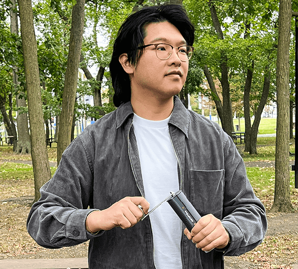 Person holding a manual coffee grinder in a park setting