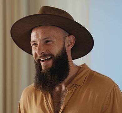 Man wearing a brown hat and shirt, smiling indoors.
