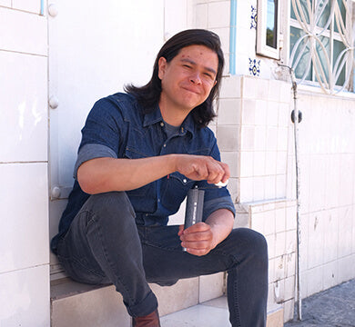 Person sitting on a step holding a manual coffee grinder with a white wall and door in the background