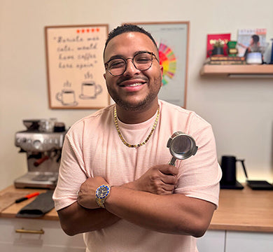 Man in a pink shirt holding a coffee scoop in a coffee shop setting