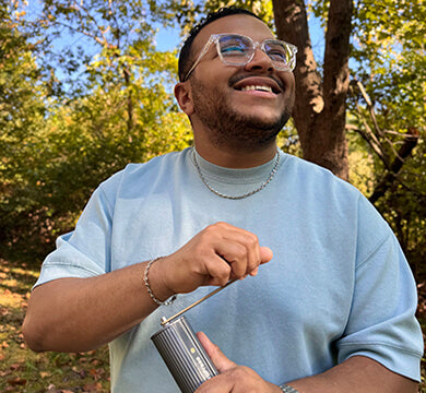 Man using a manual coffee grinder outdoors with trees in the background