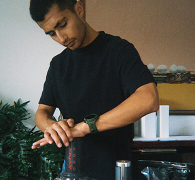 Man preparing a drink using a manual coffee grinder in a kitchen setting