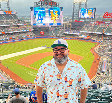 Man standing in front of a baseball stadium with a scoreboard in the background