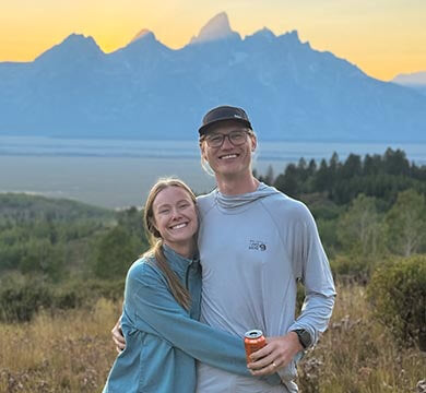 Two people hugging with a scenic mountain backdrop during sunset.