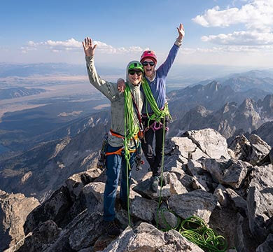 Two climbers celebrating on a mountain peak with a scenic view of mountains and sky.
