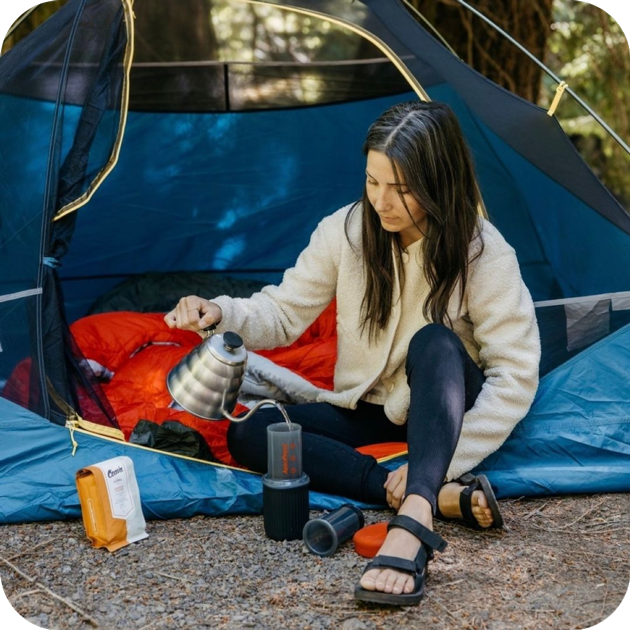 Woman by tent brewing with AeroPress Go