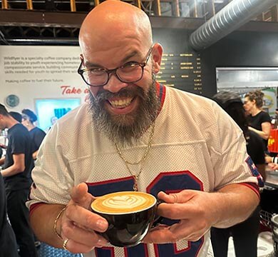 Man with a beard and glasses holding a coffee cup in a coffee shop setting
