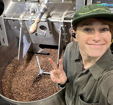 Person in a coffee roasting plant with roasted coffee beans and machinery.