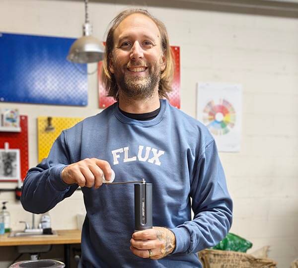 Man holding a manual coffee grinder in a workshop setting.