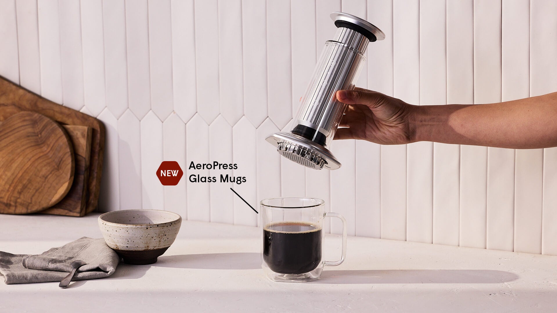 Person using an AeroPress Premium to make coffee in a glass mug on a white surface.