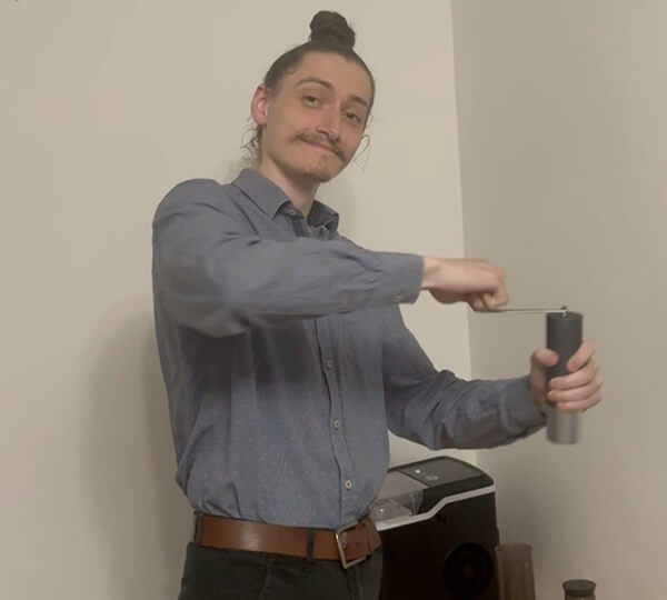 Man in a blue shirt using a manual coffee grinder indoors.