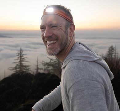 Man wearing a headlamp with a scenic background of trees and fog