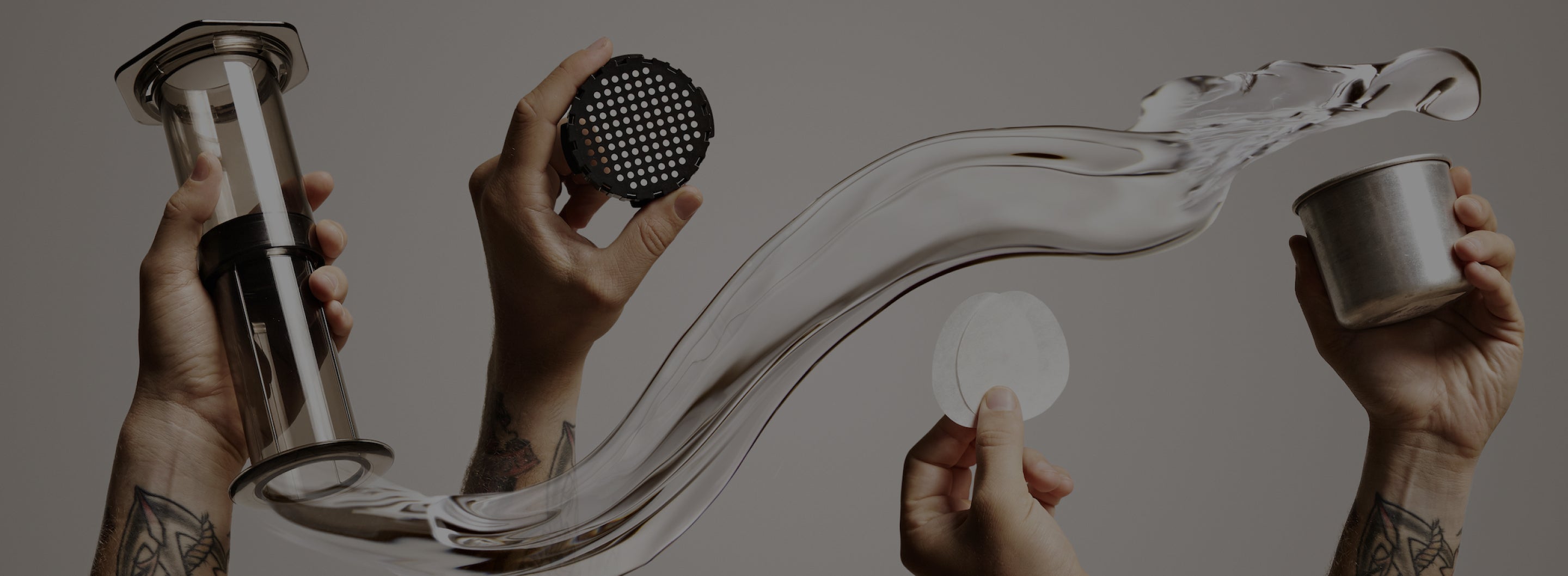 Hands holding up AeroPress Original and accessories among swirl of water