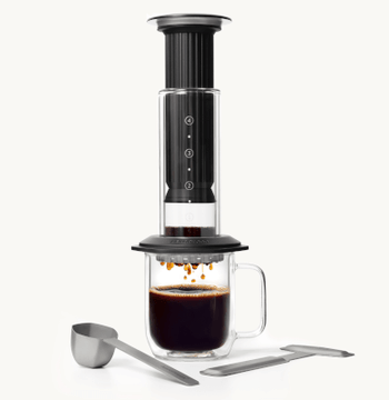 Black AeroPress Premium with a glass mug filled with coffee on a white background