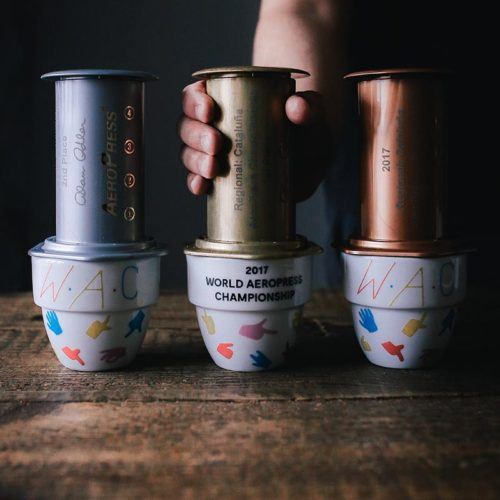 Hand holding 2017 AeroPress trophies on top of mugs